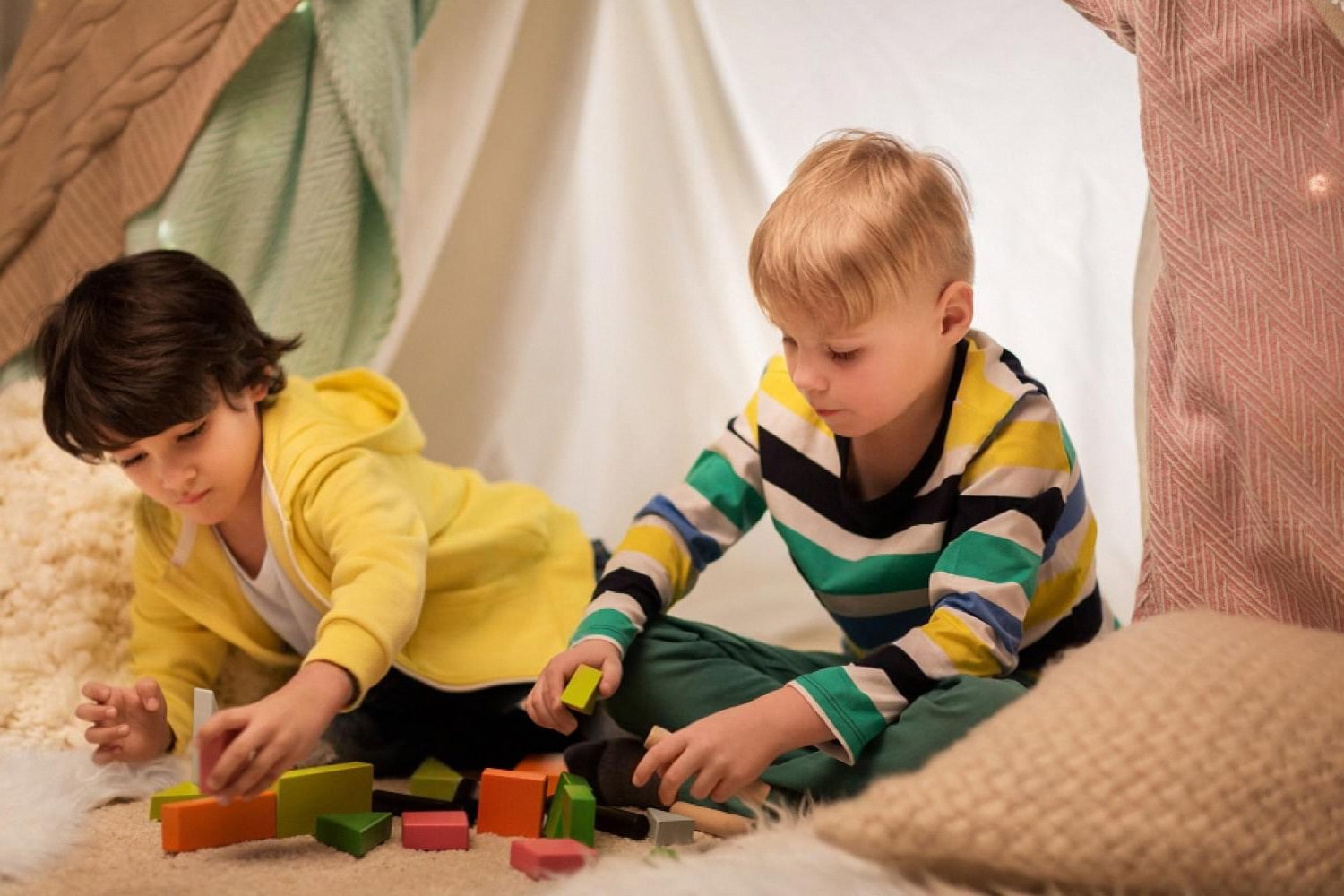 Two young children playing with colourful wooden STEM blocks inside a play tent
