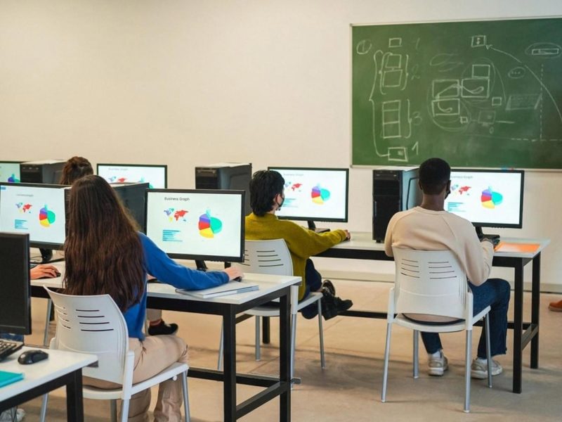 Elementary students working on desktop computers in a UAE classroom with a teacher at the whiteboard